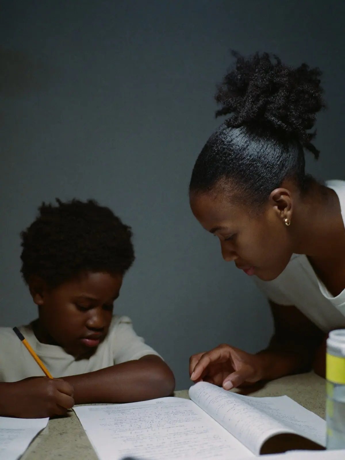 A mother helping her son with his homework at the kitchen table in the evening