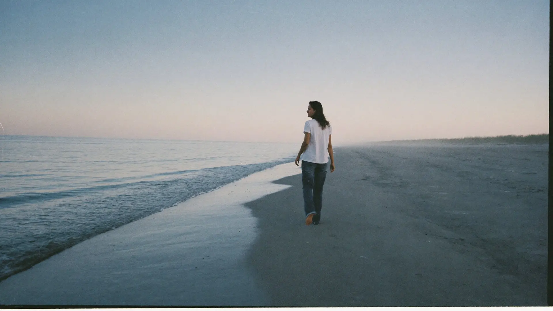 A woman walking alone along a Long Island beach in the early morning, looking out at the water