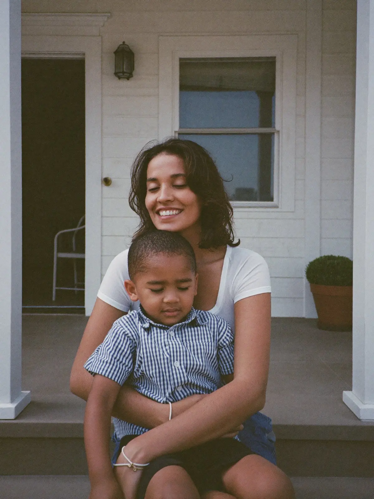 A mother holding her young son close on the front steps of their home