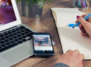Laptop, smartphone, and notebook on wooden desk.